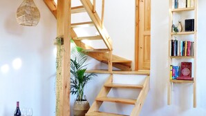 Una scala in legno dal design rustico, un tavolino con una bottiglia e dei bicchieri, e una libreria con libri.