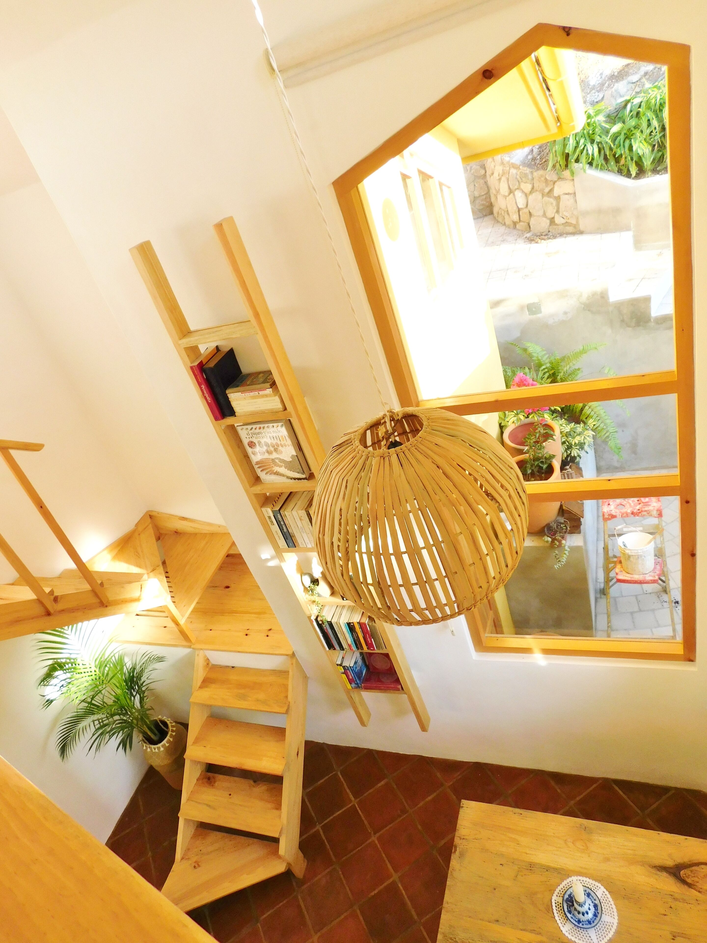 A wooden staircase leading to a balcony with a view of a garden and a window with a yellow frame.
