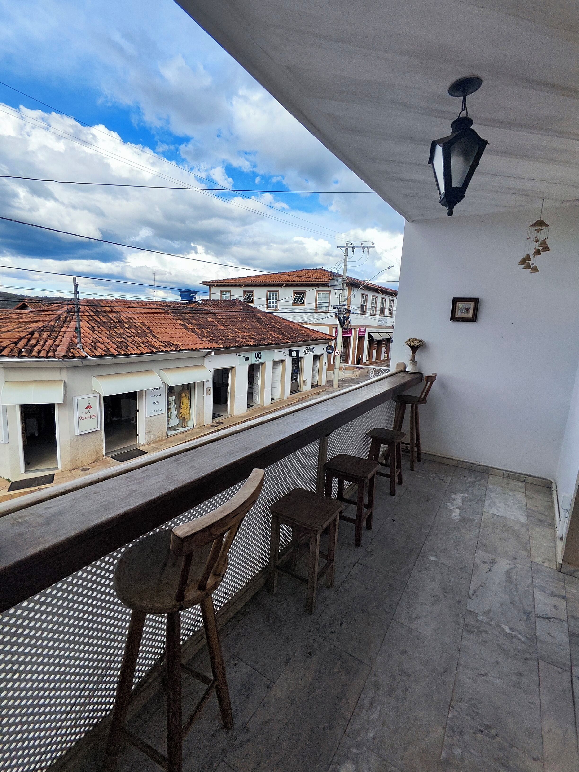 Un balcón con vistas a edificios, un farol colgante y una zona de bar con taburetes.