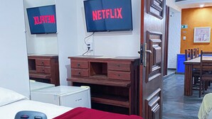 A hotel room with a bed, a desk, a dresser, a mirror, and a television displaying the Netflix logo. - Pousada Flor de Lis  (Diamantina)