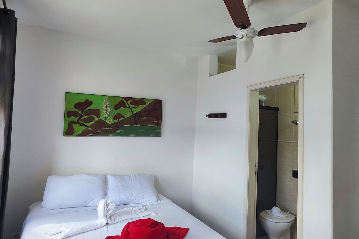 A hotel room with a bed, a ceiling fan, a painting, and a bathroom visible through an open door.