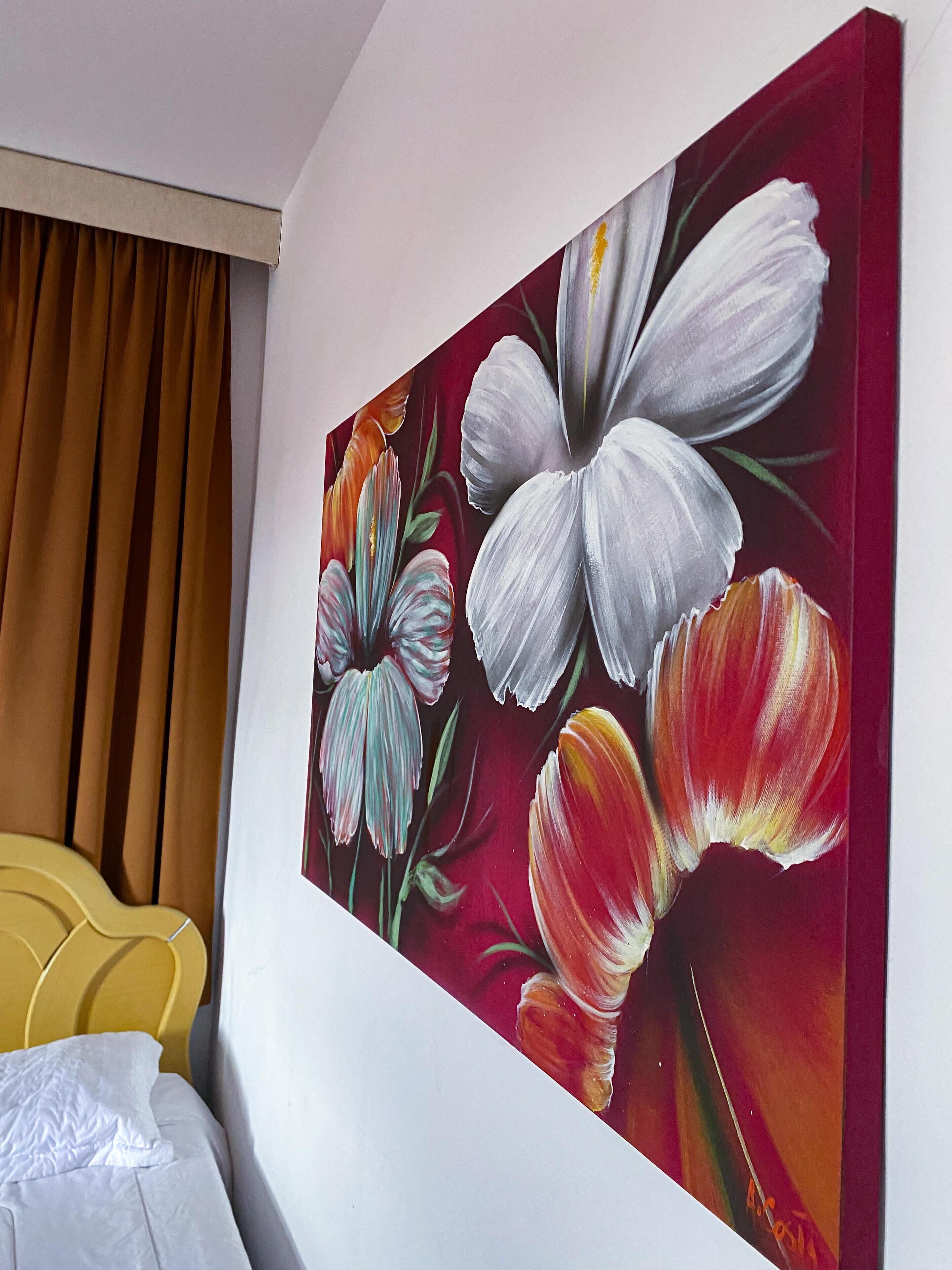 Een hotelkamer met een groot bloemenkunstwerk aan de muur, een geel hoofdeinde en een bruin gordijn.