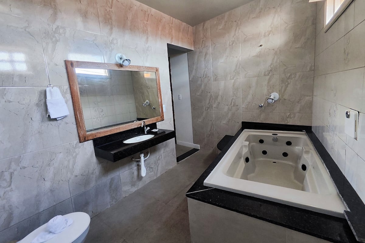 A bathroom with a marble wall, a sink with a mirror, a toilet, and a bathtub.