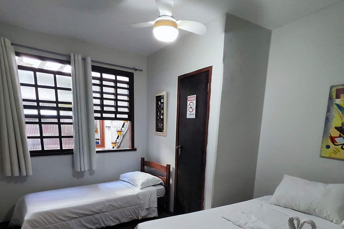 A room with two single beds, a ceiling fan, a window with blinds, and a door with a 'No Smoking' sign.