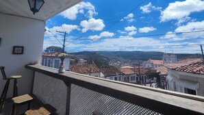 A balcony with a view of a town, including buildings with red-tiled roofs and a church. - Pousada Flor de Lis  (Diamantina)