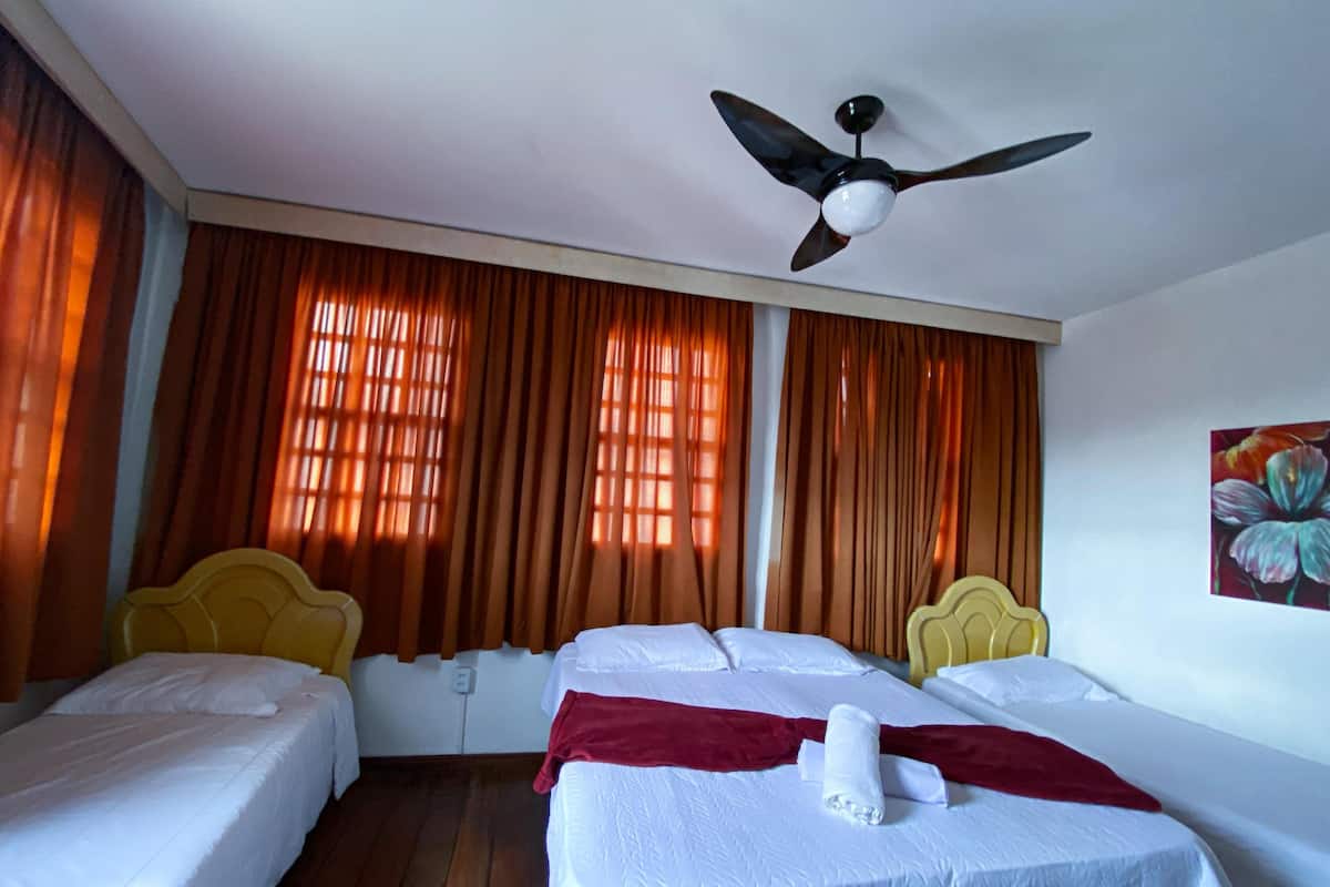 A hotel room with two single beds, a ceiling fan, and large windows with curtains.