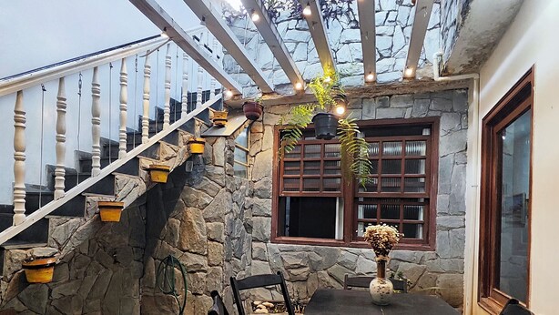 A stone wall with a wooden staircase, a dining table with chairs, and hanging plants. - Pousada Flor de Lis  (Diamantina)