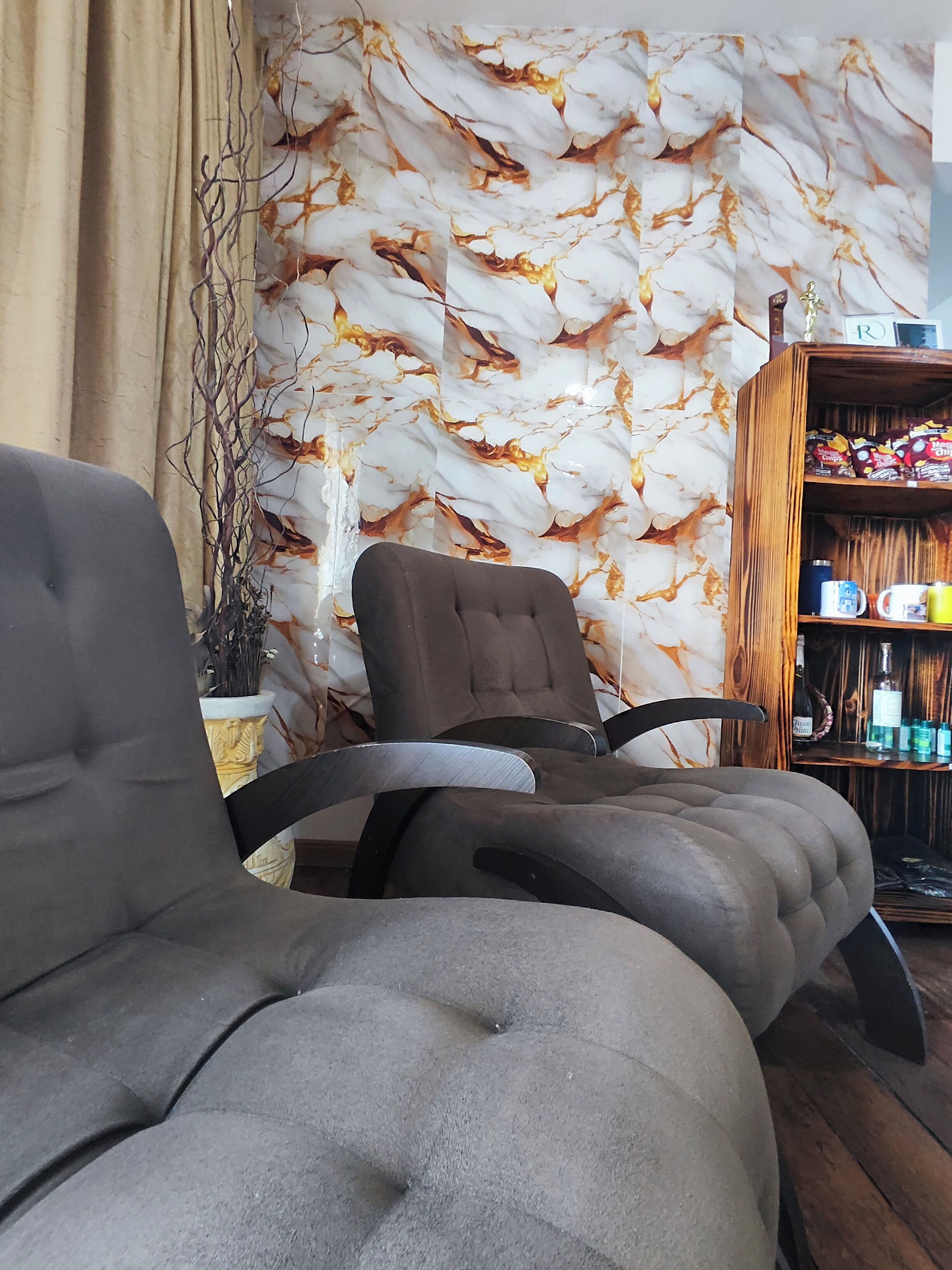 Une pièce avec un mur décoré d’un motif imitant le marbre, une bibliothèque en bois et un fauteuil recouvert d’un tissu gris.