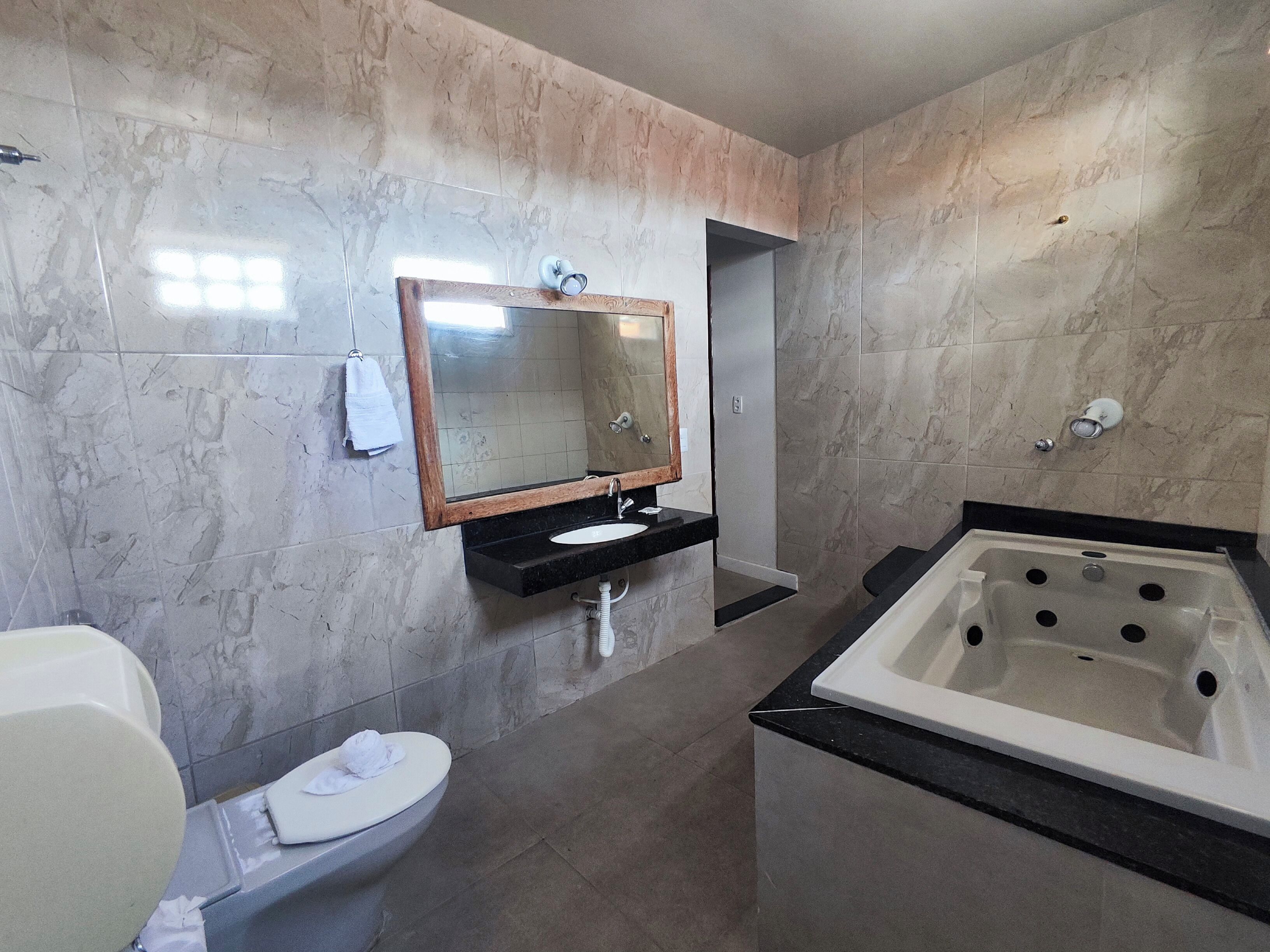 A modern bathroom with a marble wall, a sink, a toilet, a bathtub, and a mirror.