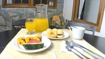 Una mesa de desayuno con una fuente de sandía en rodajas, una jarras de jugo de naranja, un vaso de jugo de naranja y una fuente de cuajada.