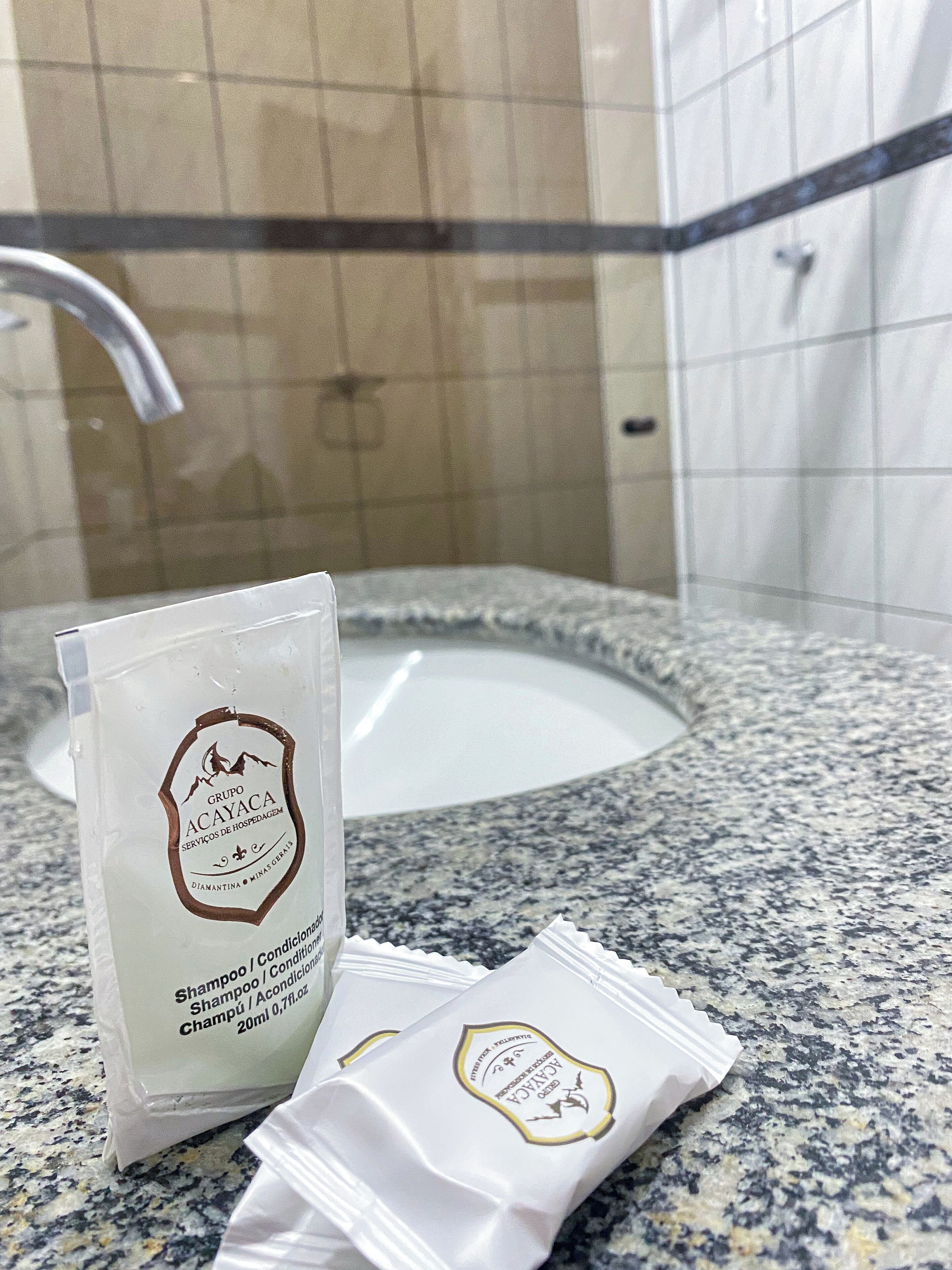 A bathroom with a granite countertop, a white sink, and a mirror. There is a bag of shampoo and conditioner on the counter.