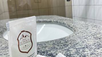 A bathroom with a granite countertop, a white sink, and a mirror. There is a bag of shampoo and conditioner on the counter.