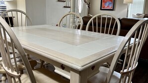 Un coin repas avec une table rectangulaire et quatre chaises, un escalier en arrière-plan et un tableau encadré au mur.