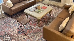Un salon avec un canapé en cuir marron, une table basse avec des livres, une cheminée et un téléviseur fixé au mur.
