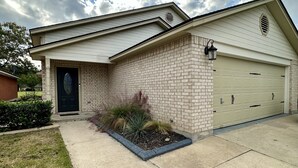 Une maison d’habitation avec une façade en briques, une porte d’entrée sombre et une porte de garage.