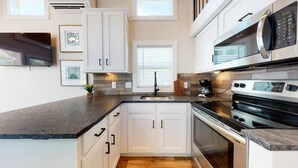 Una cocina moderna con armarios blancos, microondas integrado, estufa y cafetera.