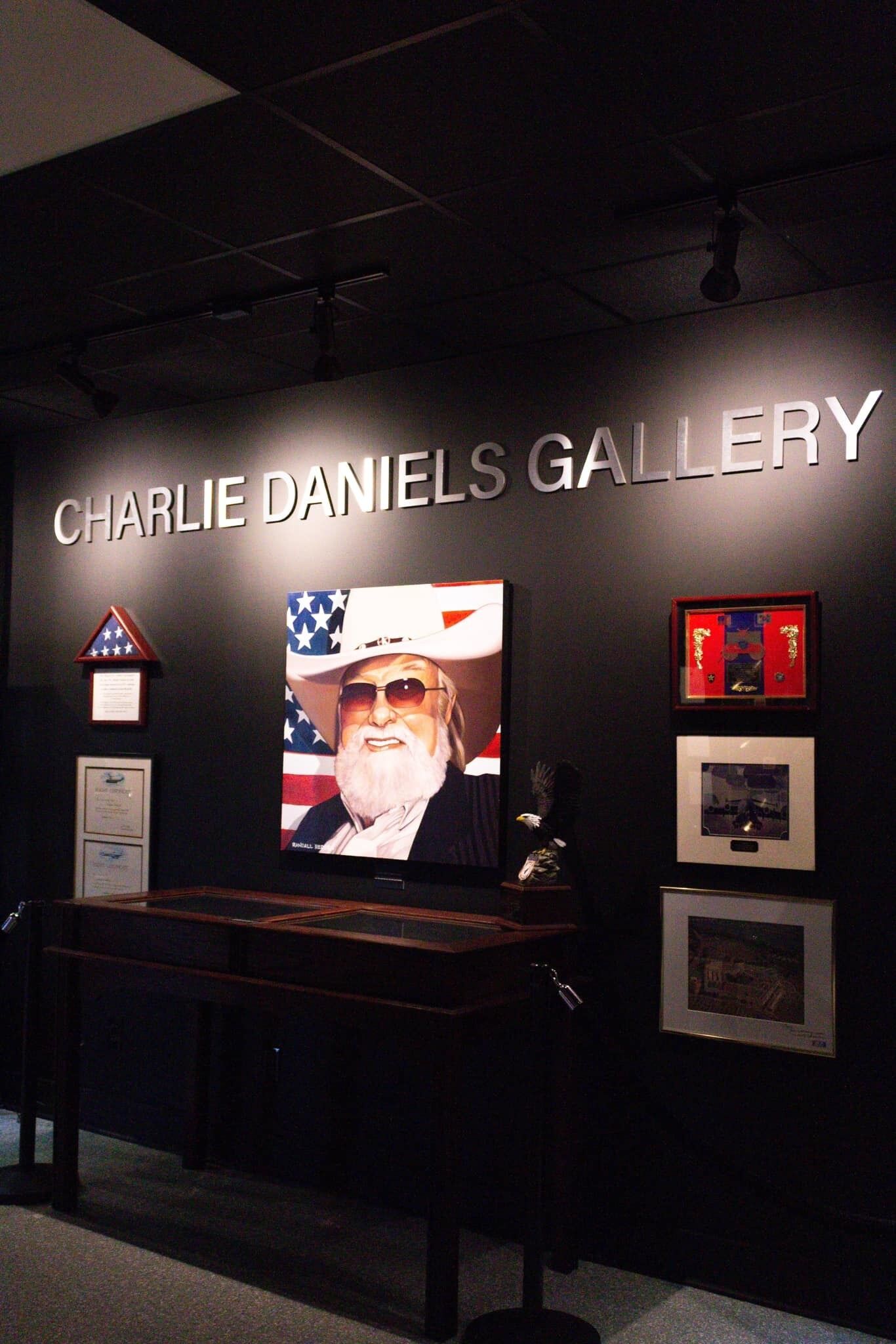 Une galerie où est exposé un grand portrait ainsi que divers objets encadrés.