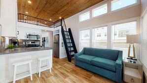Una cocina moderna con armarios blancos, una estufa de acero inoxidable y una escalera negra que lleva a un nivel superior.