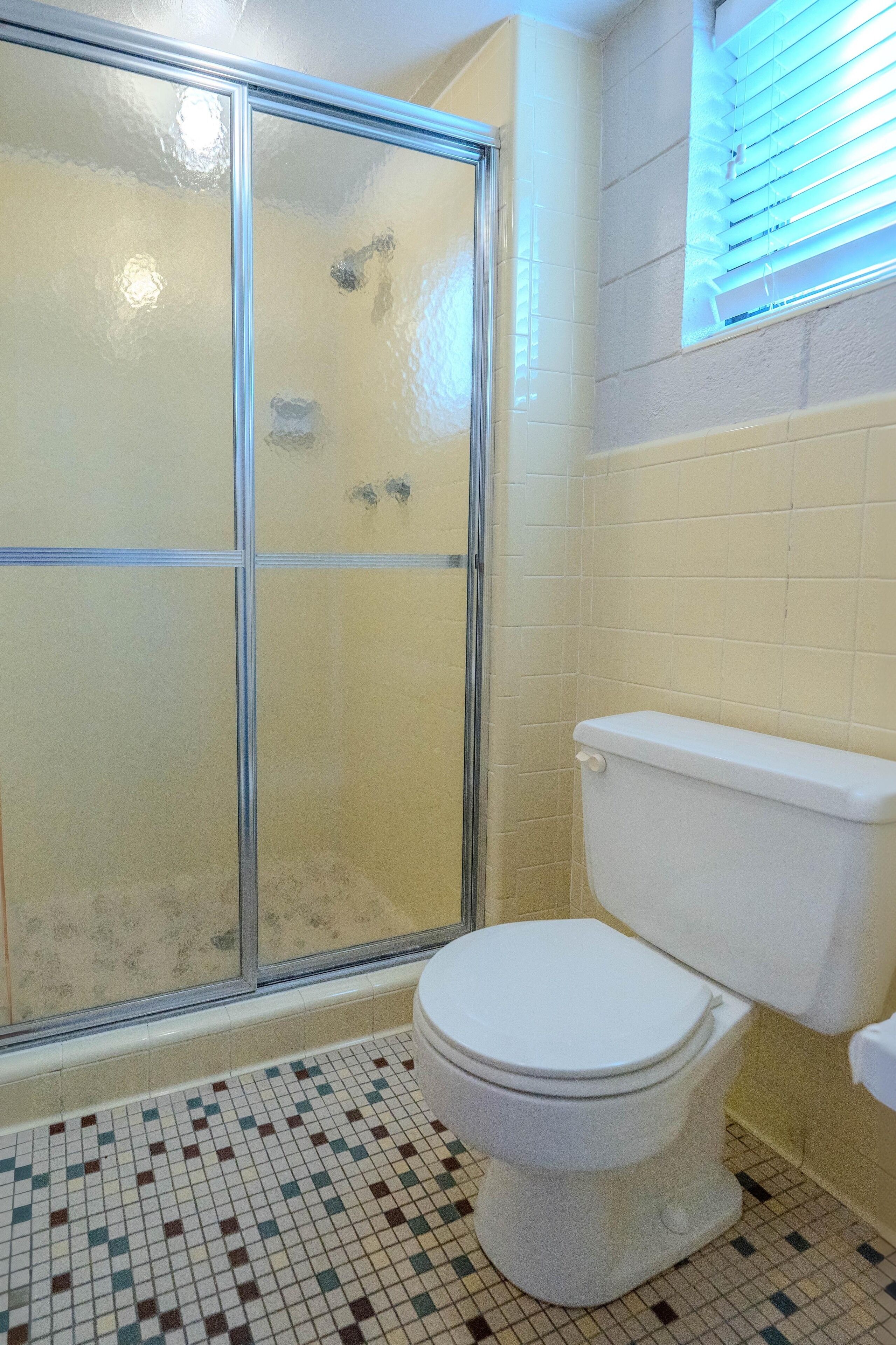 A bathroom with a glass shower enclosure, a white toilet, and a tiled floor.