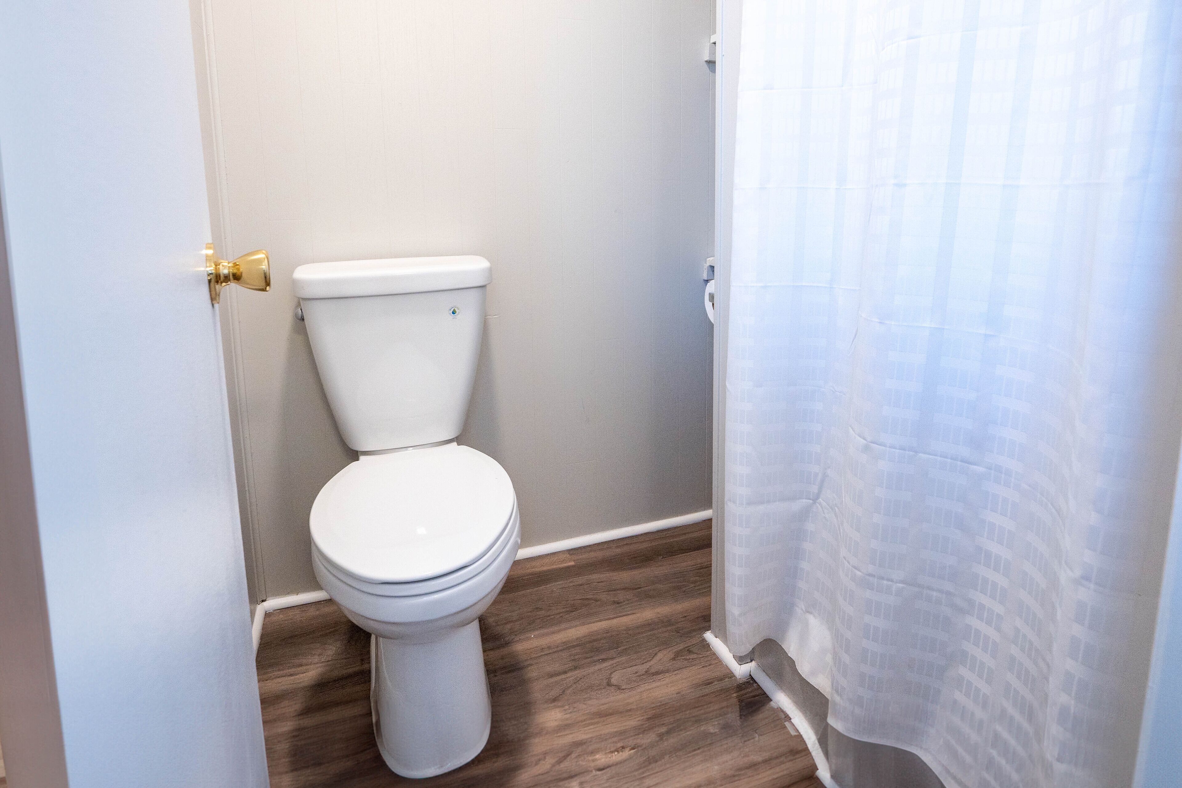 Une salle de bain avec des toilettes blanches, un plancher en bois et un rideau de douche.