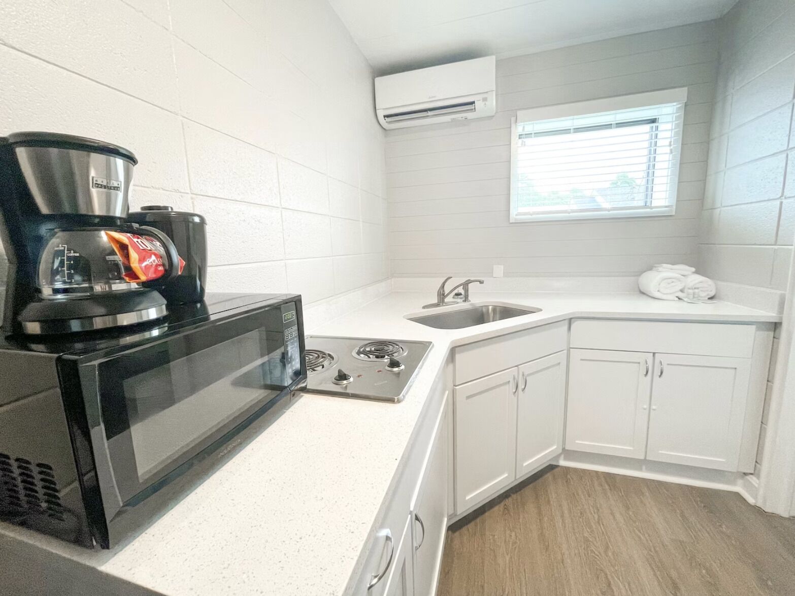 A compact kitchen with a microwave, stove, sink, and white cabinets.