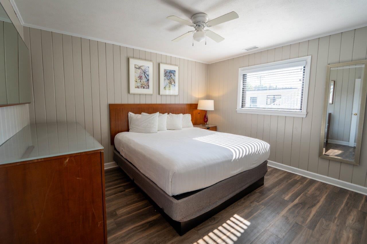 A bedroom with a bed, wooden headboard, bedside lamp, and a ceiling fan.