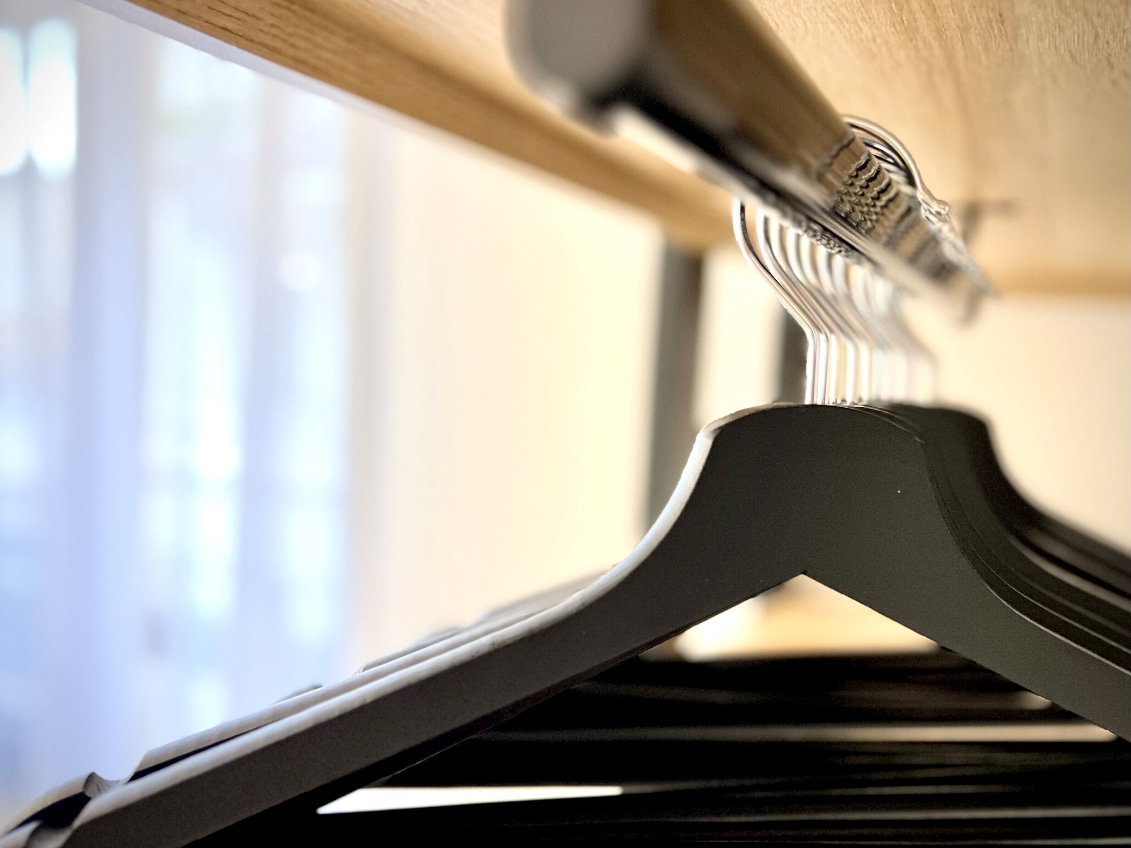 A close-up of a metal rack with a coat hanging on it, positioned under a wooden beam.