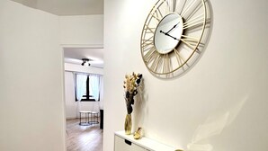 Een hal met een witte console tafel, een gouden klok aan de muur en een vaas met gedroogde bloemen.