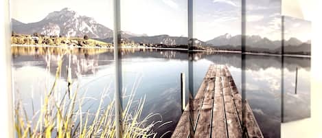 Ein weiter Blick auf einen See mit Bergen im Hintergrund und einem Holzsteg, der ins Wasser führt.