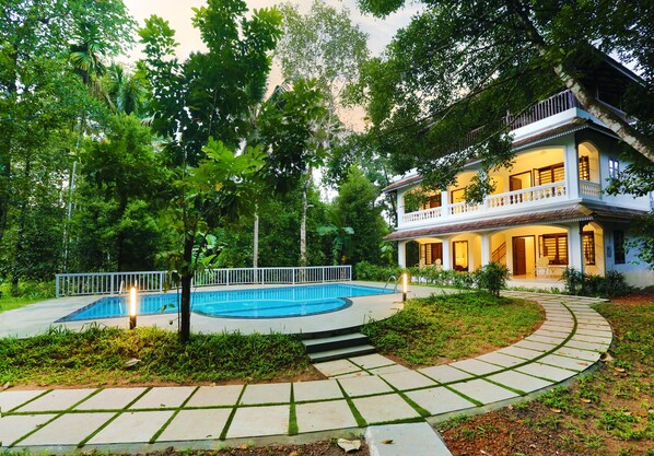 A two-story house with a swimming pool, surrounded by lush greenery and a well-maintained garden. - Once Upon The River (Aluva)