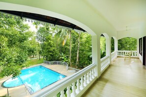 A pool area with a view of lush greenery, a covered balcony with a railing, and a wooden floor. - Once Upon The River (Aluva)