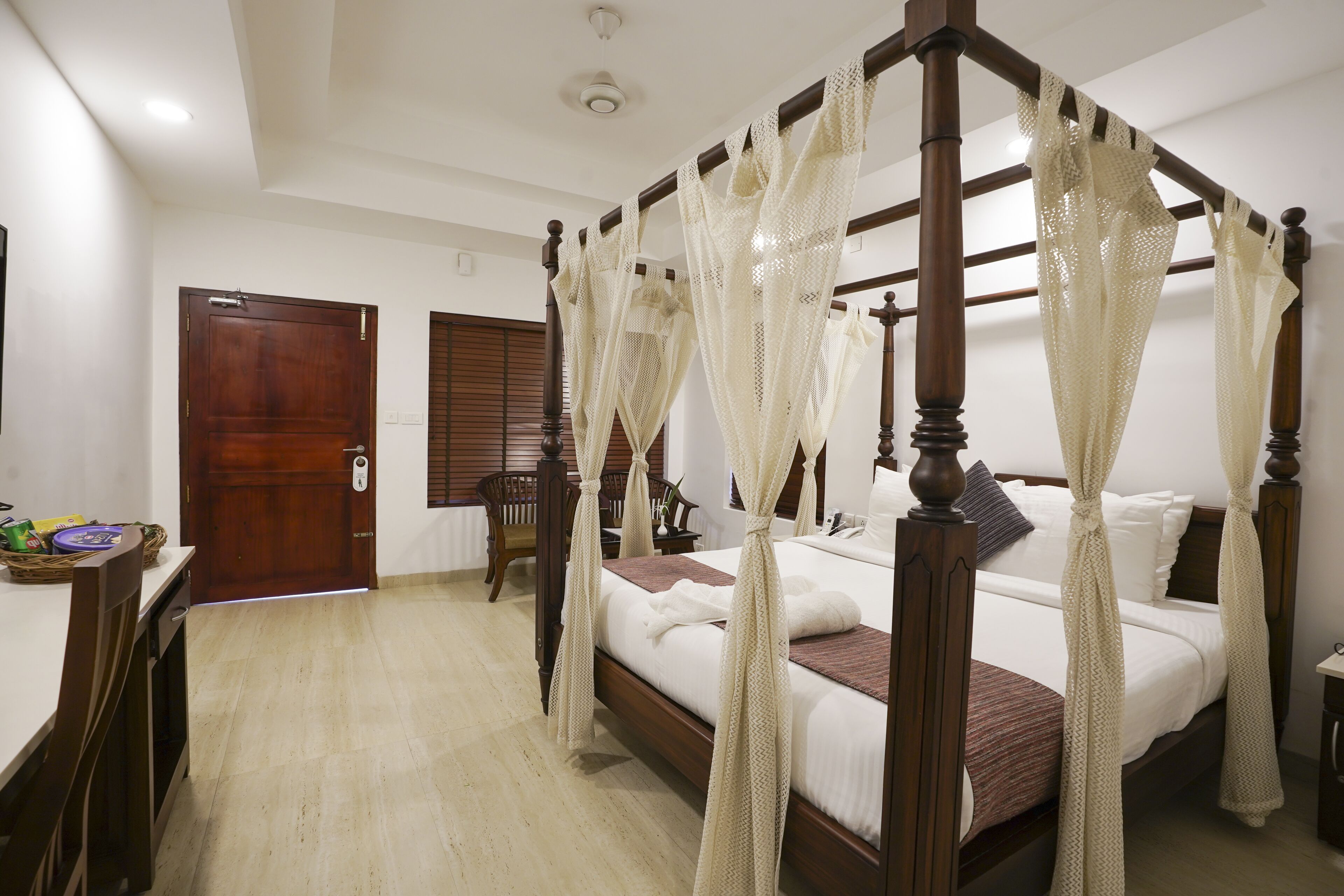 A four-poster bed with a canopy, a wooden desk with a chair, and a wooden door.