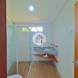 A bathroom with a glass shower enclosure, a sink with a granite countertop, and a wooden vanity.