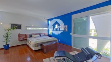 Quarto com cama, cadeira de massagem, planta em vaso e uma janela grande.