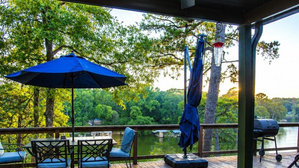 Une terrasse en bois avec des meubles d’extérieur, un ventilateur de plafond et une vue sur un lac.