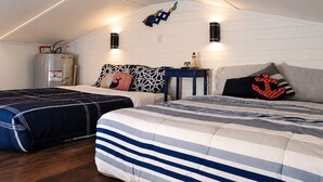 Une chambre avec un plafond en pente, un lit avec une literie à rayures, une table de chevet, un radiateur et un luminaire fixé au mur.