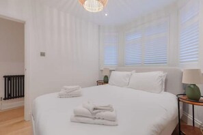 Een hotelkamer met een groot bed, nachtkastje, lamp en een raam met zonwering.