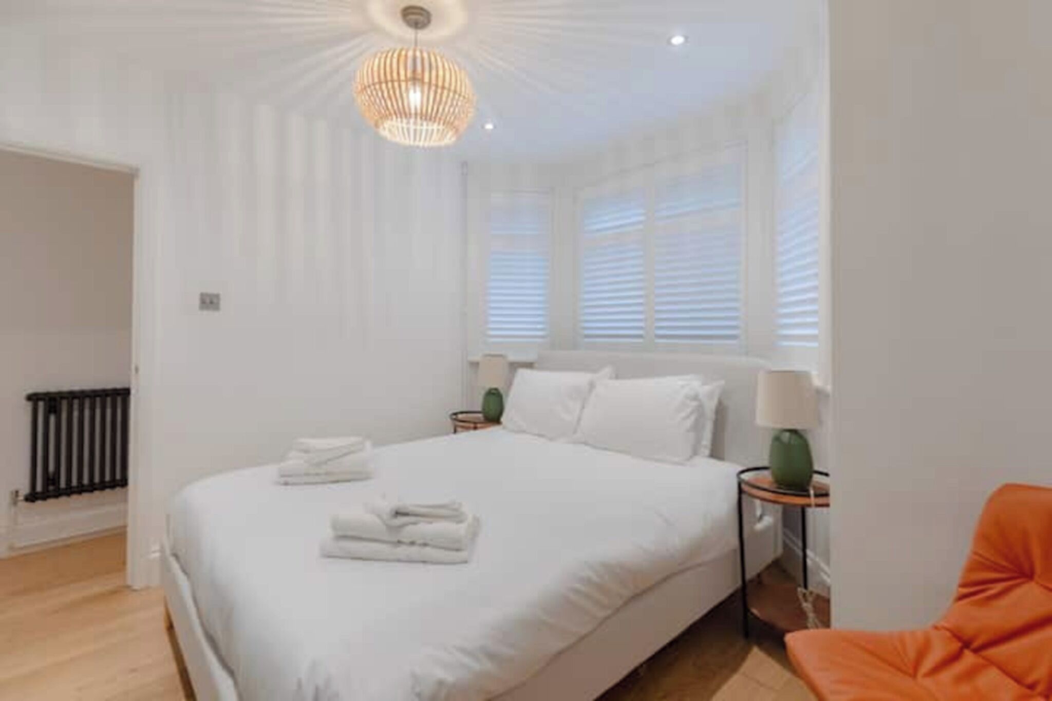 A hotel room with a large bed, two bedside tables with lamps, a window with blinds, and a wooden floor.