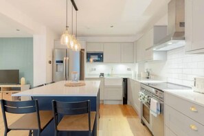 Een moderne keuken met een centraal eiland, roestvrijstalen apparatuur en hanglampen.