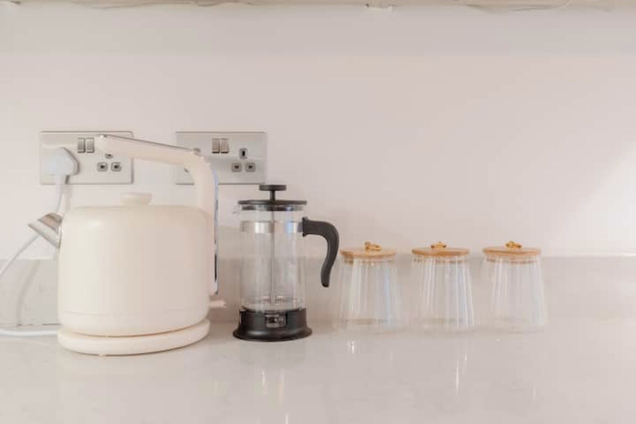 A kitchen with a white countertop, a coffee maker, a glass carafe, and four jars with lids.