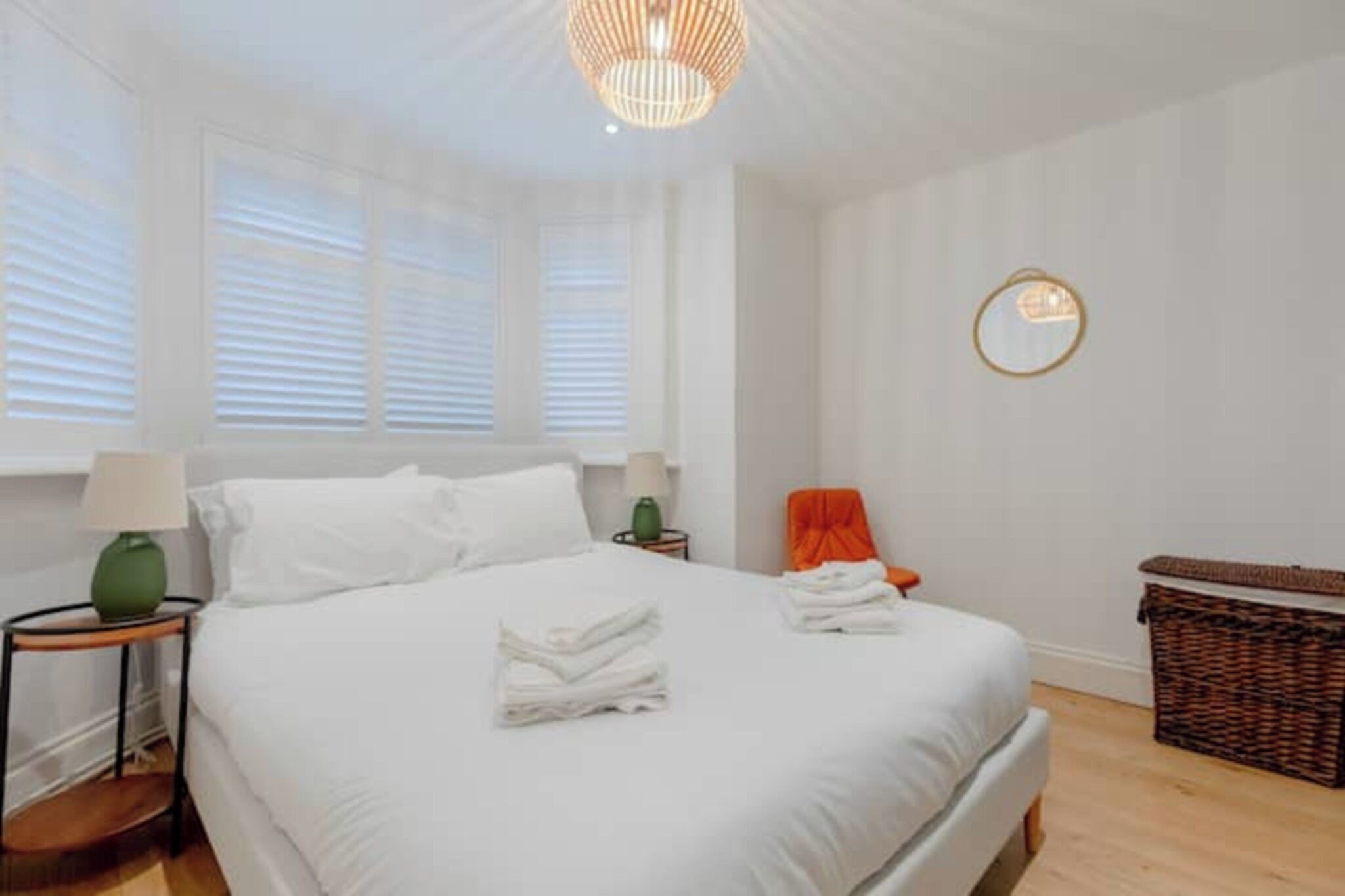 A bedroom with a bed, a nightstand, a lamp, a chair, and a basket.