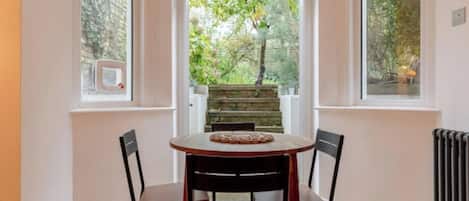 Un coin repas avec une table et des chaises, une vue sur un jardin par la fenêtre et un radiateur au mur.