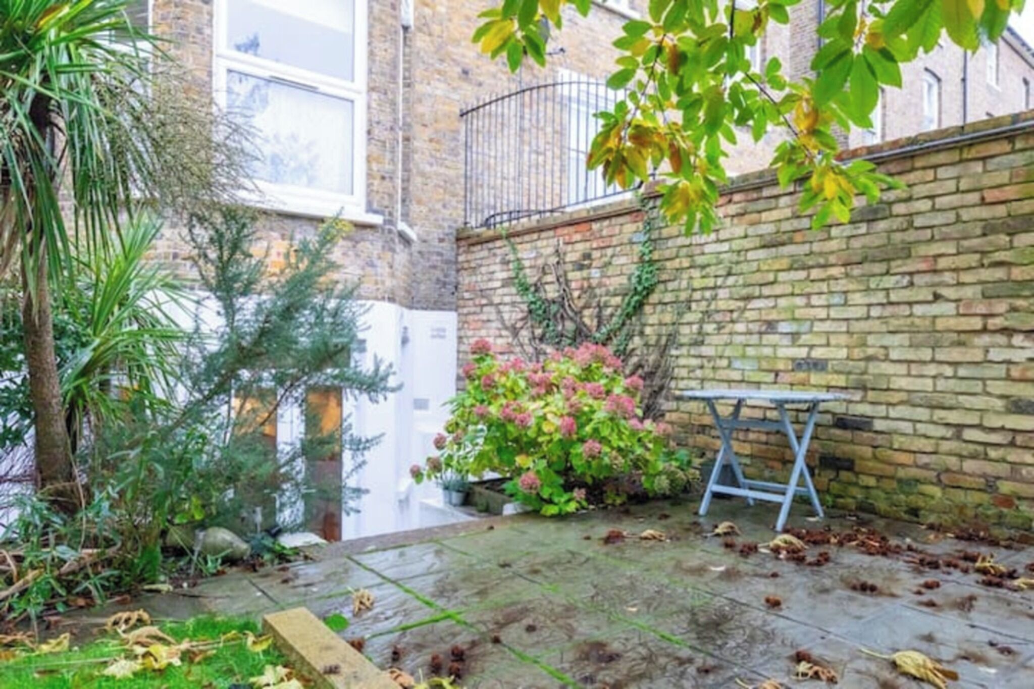 A brick building with a small garden area, a metal bench, and a potted plant.