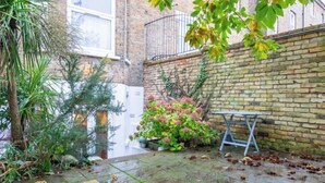 A brick building with a small garden area, a metal bench, and a potted plant. - Stylish Garden Home 2 BDR Wimbledon (London)