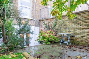 A brick building with a small garden area, a metal bench, and a potted plant. - Stylish Garden Home 2 BDR Wimbledon (London)