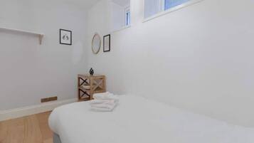 A bedroom with a bed, a small wooden side table, and a window.