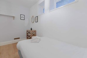 A bedroom with a bed, a small wooden side table, and a window.