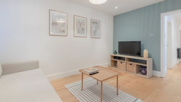 A modern living room with a sofa, a coffee table, and a TV on a stand. - Stylish Garden Home 2 BDR Wimbledon (London)