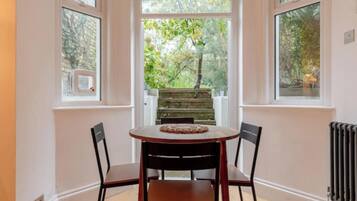 A dining area with a table and chairs, a view of a garden through a window, and a radiator on the wall.