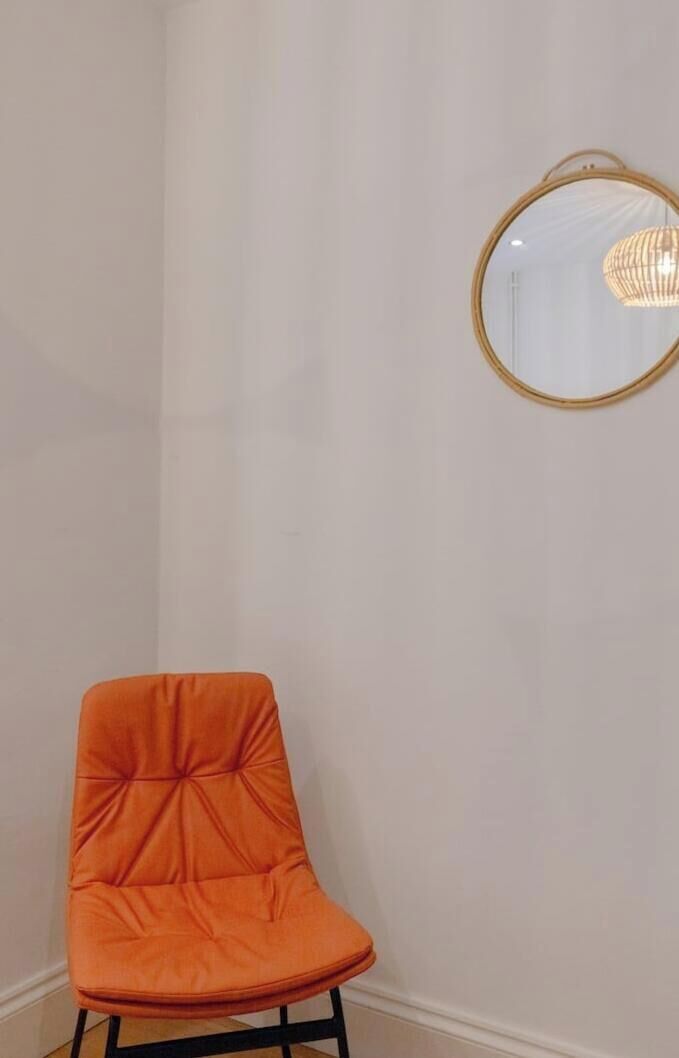 A corner of a room with a single orange chair and a round mirror on the wall.